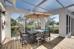 Un espace extérieur abrité, doté d’une table et de chaises, d’un parasol en chaume et offrant une vue sur le paysage environnant.