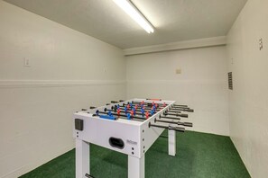 A room with a foosball table, green carpet, white walls, and a ceiling light.