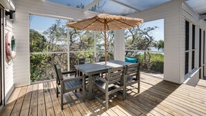 A covered outdoor deck with a table and chairs, a thatched umbrella, and a view of the surrounding trees and water. - Golf Cart, Bimini Cove by SeaBreeze Vacation (Anna Maria)