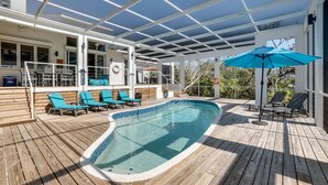 An outdoor swimming pool with blue chairs and a sun umbrella, surrounded by a wooden deck and a covered area with white railings. - Golf Cart, Bimini Cove by SeaBreeze Vacation (Anna Maria)