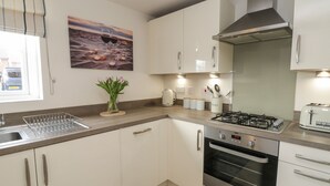 A modern kitchen with white cabinets, a gas stove, an oven, and a window with a view of the street. - Woodside View (Whitby)