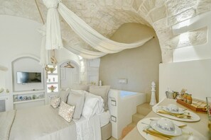 Un dormitorio con cama, televisor, tocador con espejo y espacio para el desayuno.