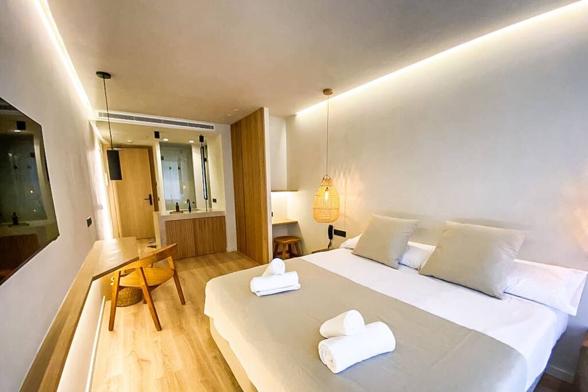 A modern hotel room with a large bed, a wooden chair, a desk, and a mirror.