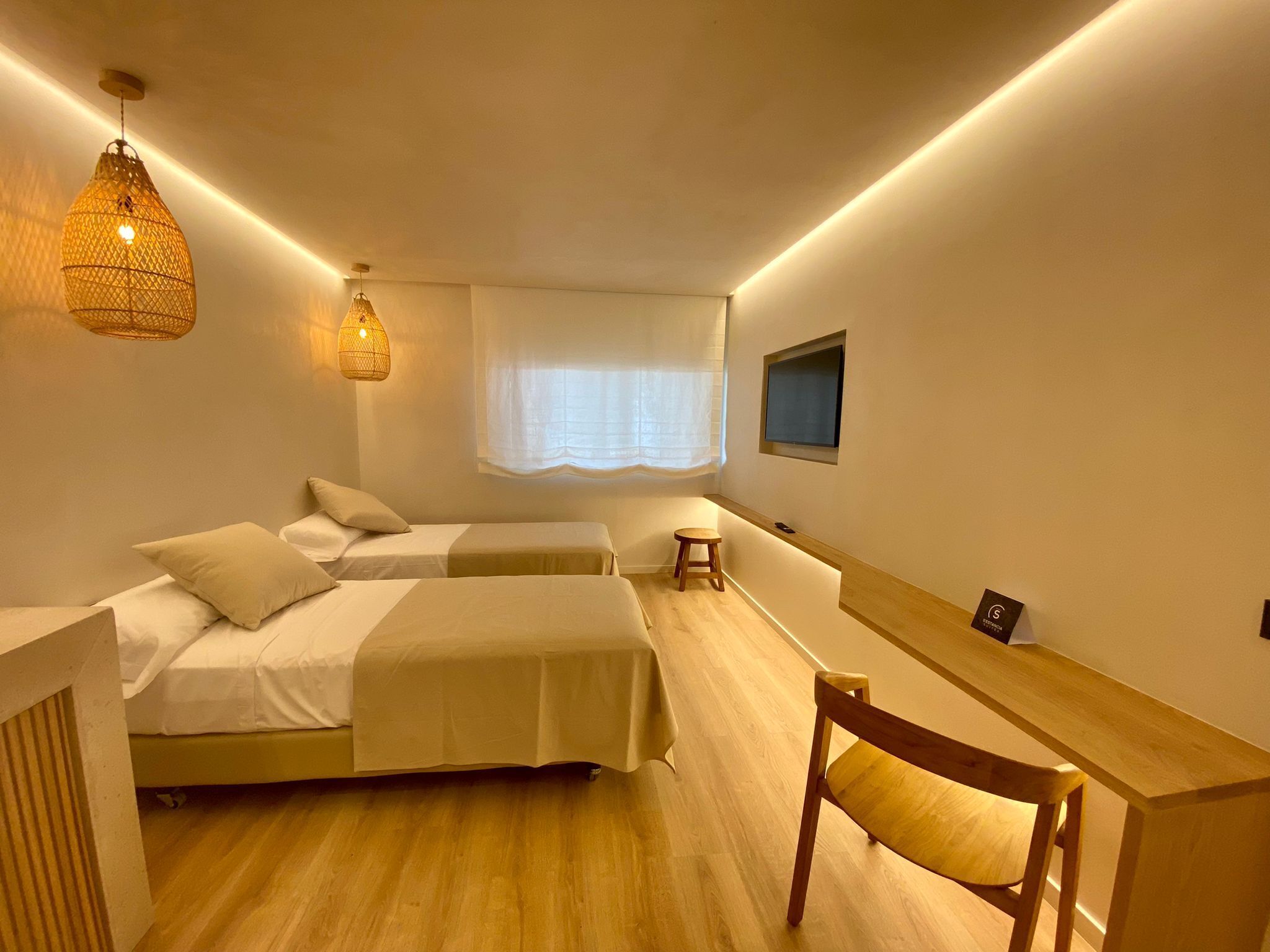 A modern bedroom with two beds, a desk, a chair, and a TV.
