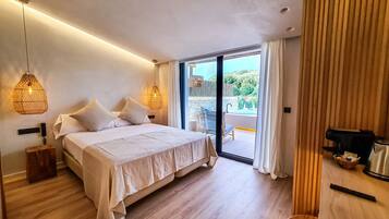 A bedroom with a bed, bedside tables, a wooden floor, and a view of a pool and greenery outside.