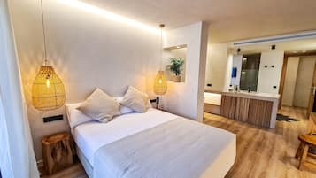 Una habitación de hotel moderna con una cama grande, dos lámparas de noche, un taburete de madera y una planta pequeña.