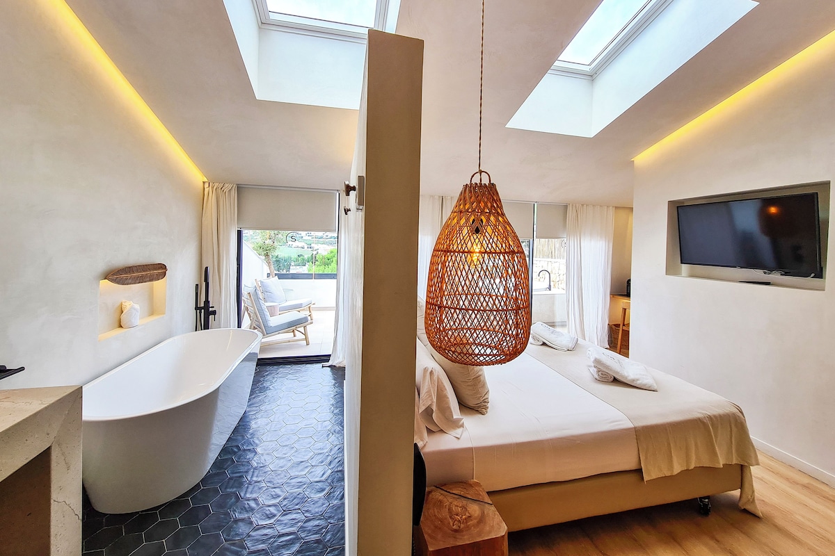 Un dormitorio moderno con tragaluz, una cama grande, televisor y baño con bañera y ducha.