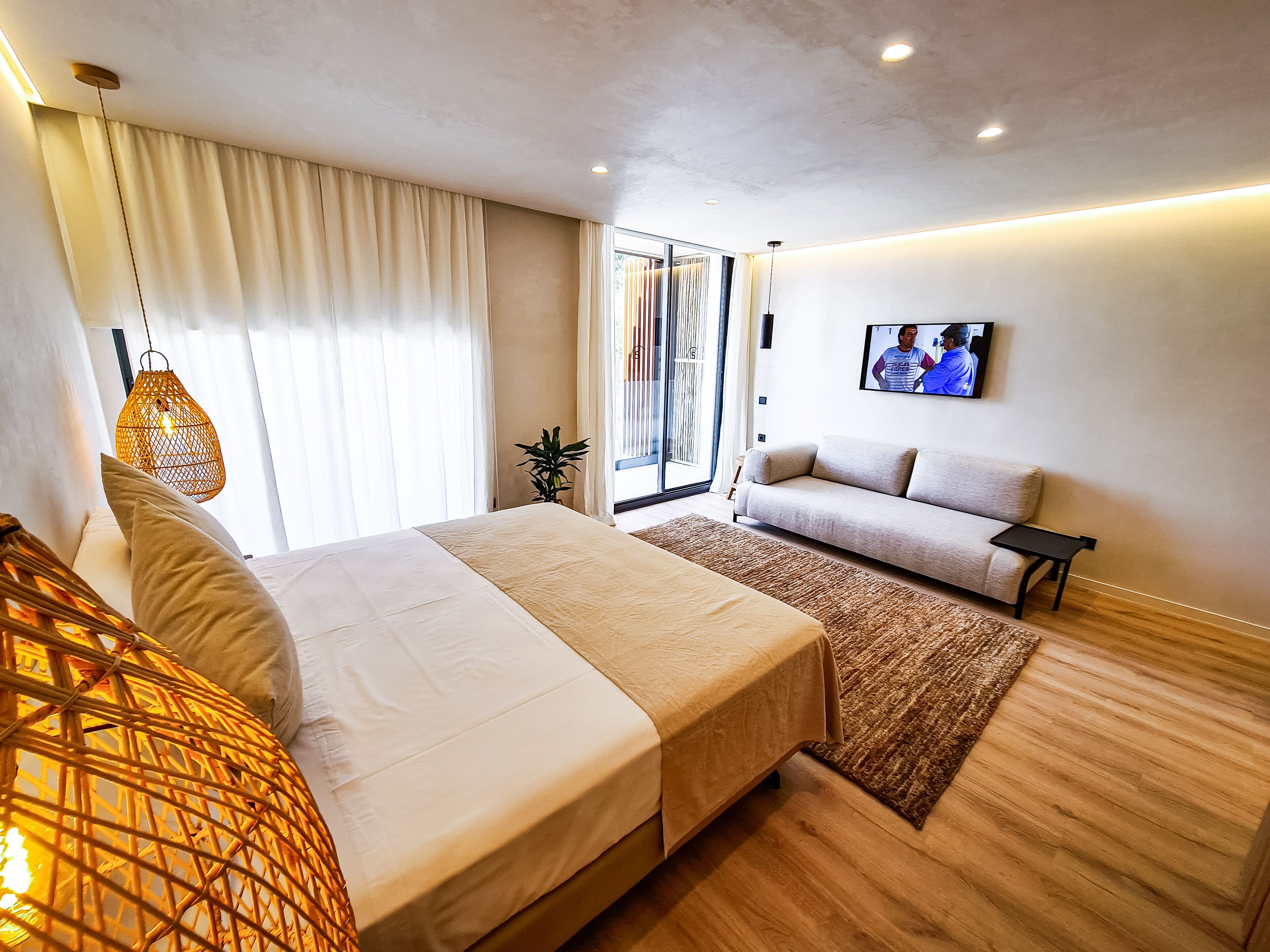 Une chambre d’hôtel moderne avec un grand lit, un canapé, un téléviseur fixé au mur et une fenêtre avec des rideaux.