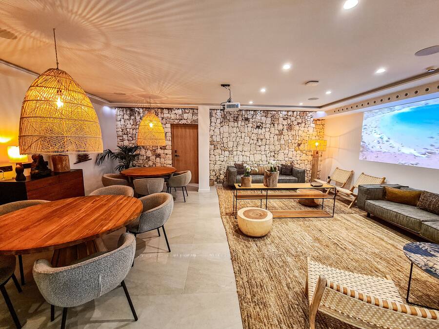 A modern living room with a stone wall, a large screen, and a dining area with a wooden table and chairs.