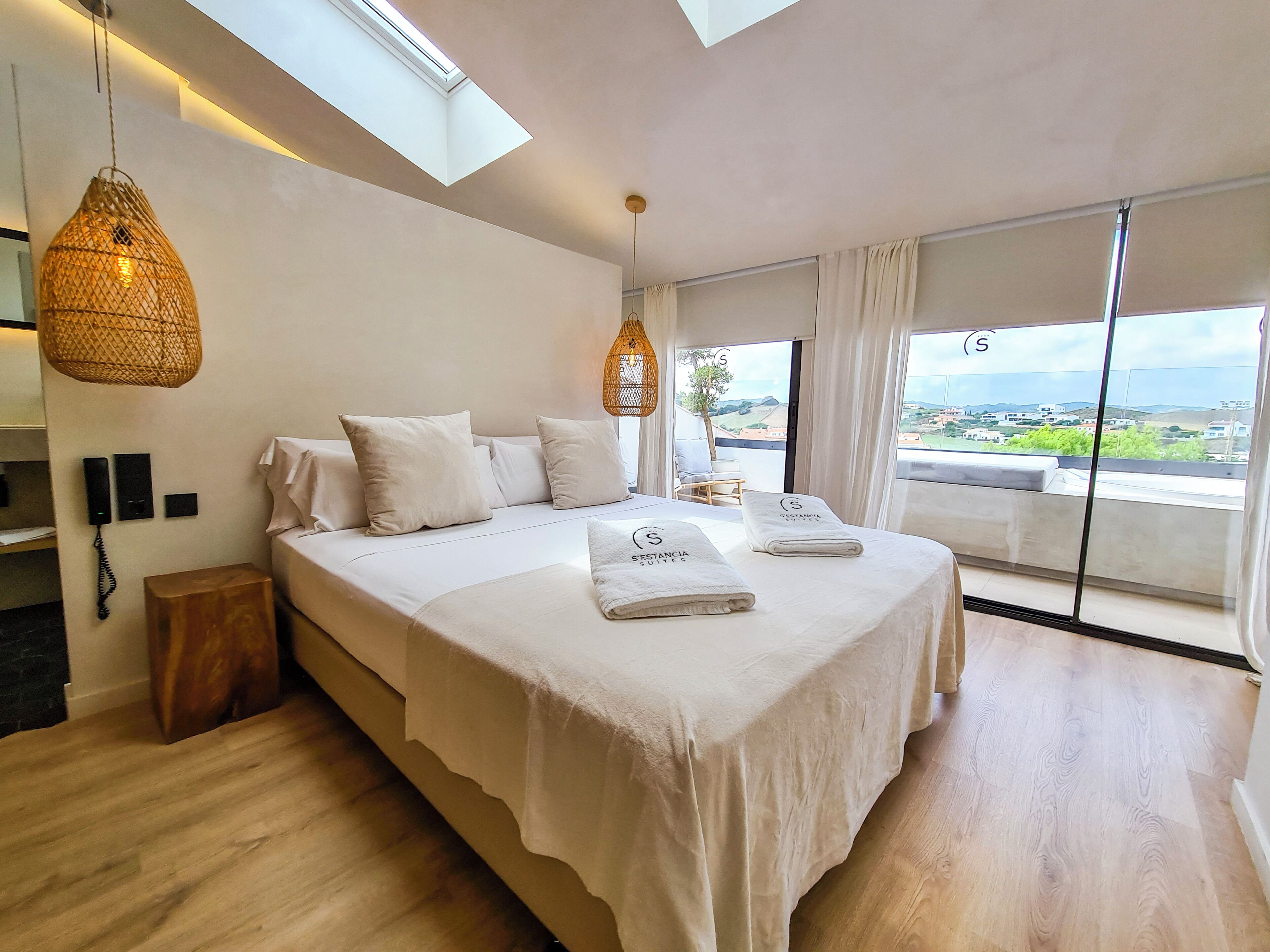 A modern bedroom with a large bed, a phone on the wall, and a view of the landscape through the window.