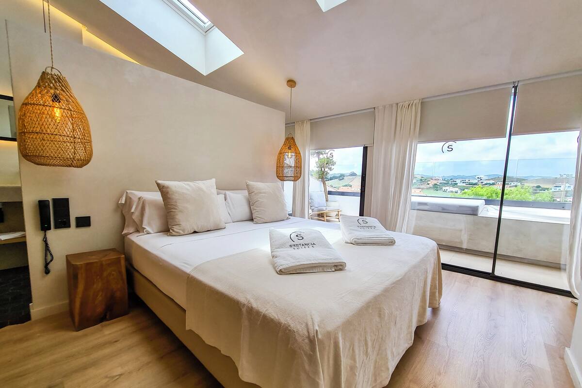 A modern bedroom with a large bed, a phone on the wall, and a view of the landscape through the window.