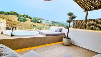 Une terrasse extérieure moderne, dotée d’un jacuzzi, d’un espace salon et offrant une vue sur la campagne.
