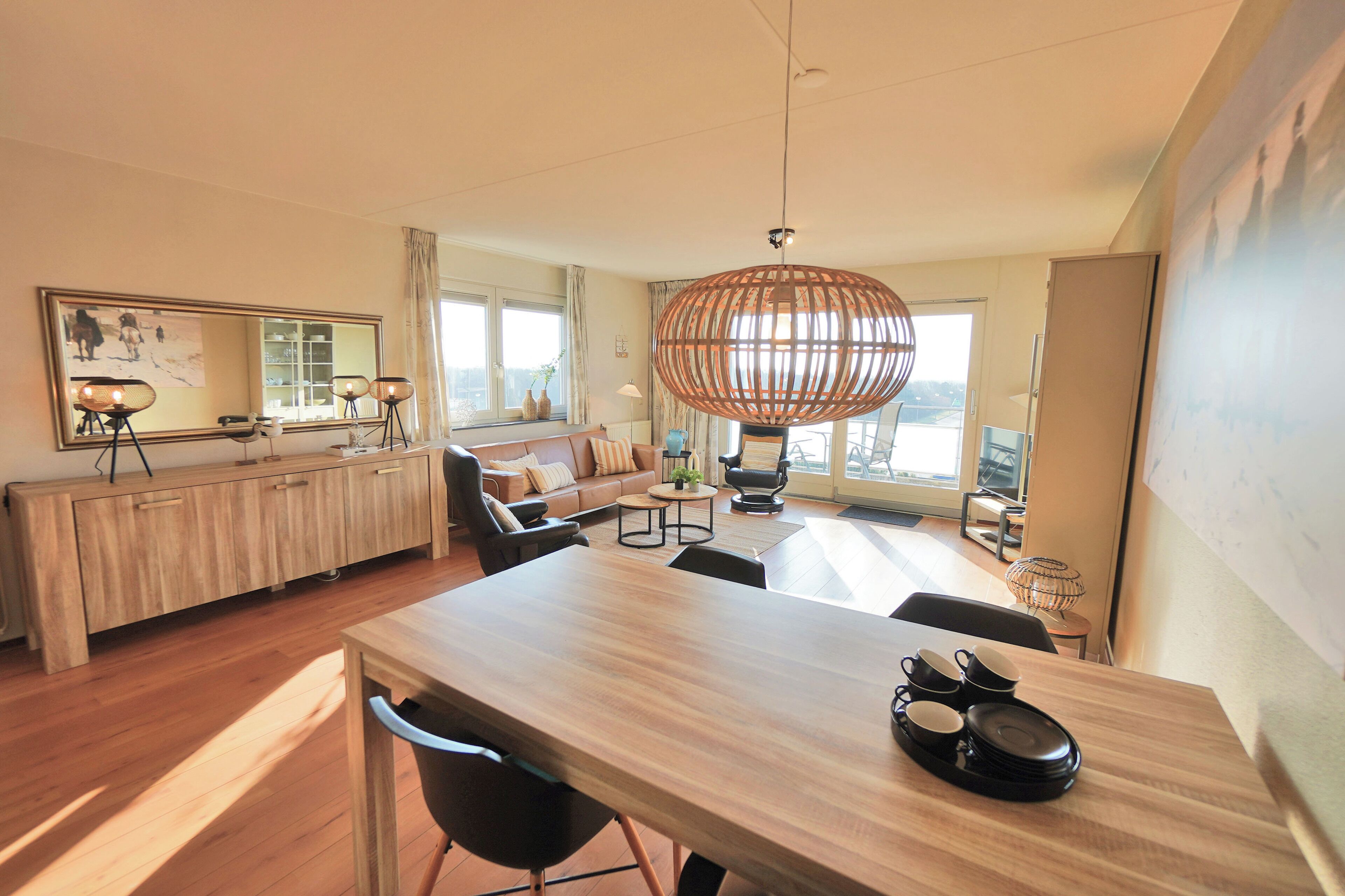 Un salon moderne avec une table à manger en bois, un grand miroir et un luminaire suspendu en rotin.