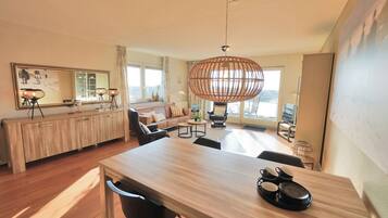 Un salon moderne avec une table à manger en bois, un grand miroir et un luminaire suspendu en rotin.
