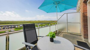 A balcony with a table, a chair, a potted plant, and a blue umbrella. - Vacation apartment right by the sea near Callantsoog LekkerNaarZee (Callantsoog)