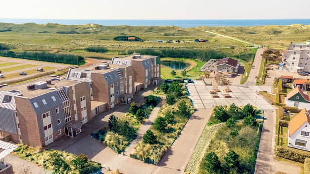 A modern building with a flat roof, surrounded by a landscaped area with pathways and greenery. - Vacation apartment right by the sea near Callantsoog LekkerNaarZee (Callantsoog)