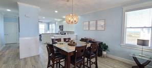 A modern kitchen with white cabinets, a central island, and a dining area with a glass table and wooden chairs.