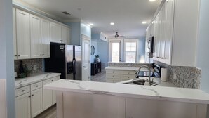 Cozinha moderna com armários brancos, geladeira preta, bancada de mármore e ventilador de teto.