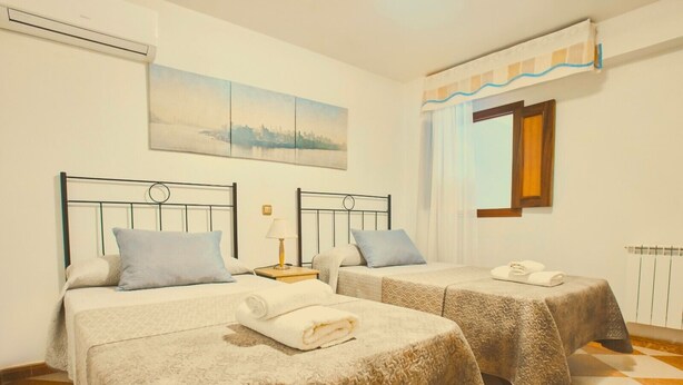 A hotel room with two beds, a painting on the wall, a window with curtains, and a radiator. - Los Mayorales Apartment (Garrovilla, La)