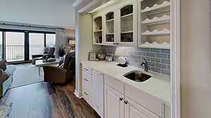 A modern kitchen with white cabinetry, a built-in sink, and a window overlooking a balcony. - Oceanfront Beach View, Large Pool, Updated! (Pawleys Island)