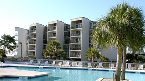 A swimming pool with lounge chairs and palm trees, surrounded by a modern building with multiple balconies. - Oceanfront Beach View, Large Pool, Updated! (Pawleys Island)