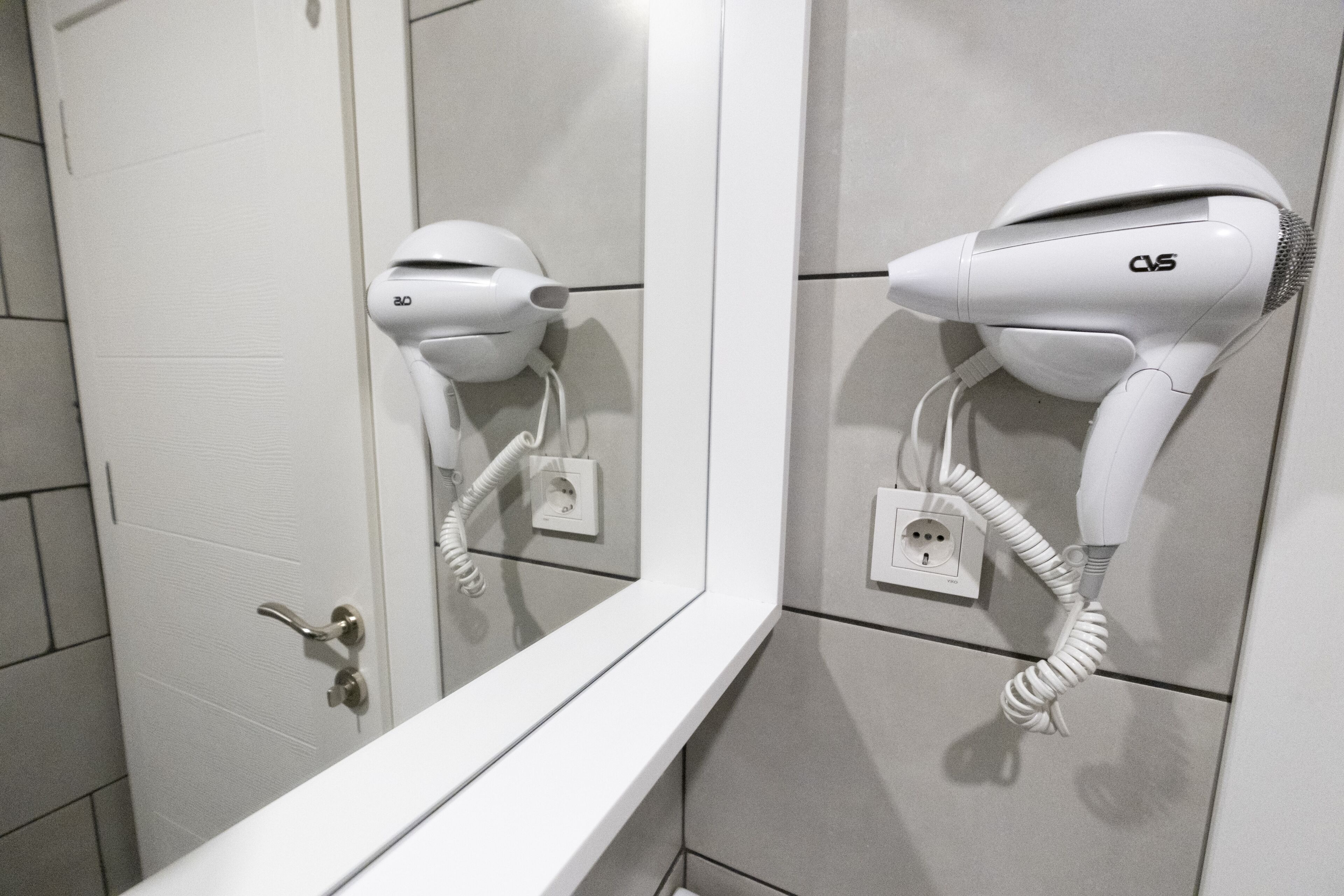 A bathroom with a white door, a mirror, and a hairdryer mounted on the wall.