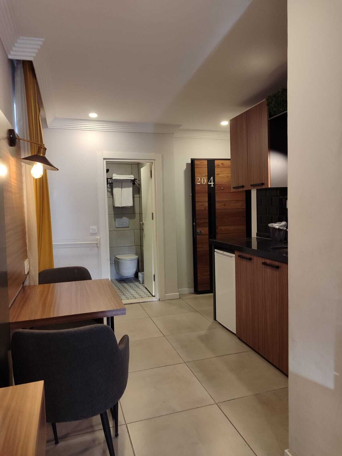 A compact kitchen with wooden cabinets, a black countertop, and a small refrigerator.