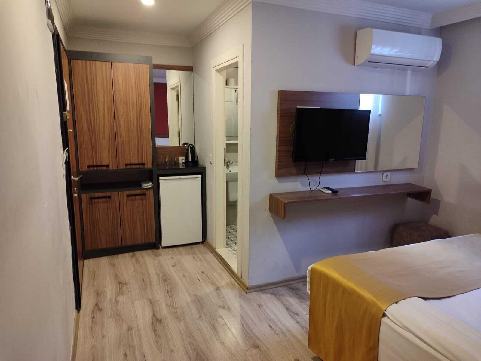 Una habitación de hotel compacta con kitchenette, una cama, un televisor y un equipo de aire acondicionado.