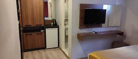 Una habitación de hotel compacta con kitchenette, una cama, un televisor y un equipo de aire acondicionado.