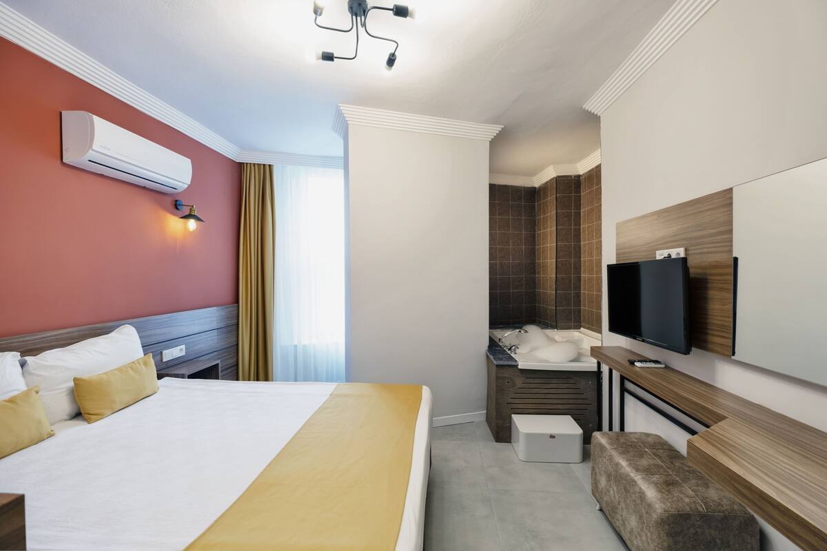 A hotel room with a large bed, a TV, a bathroom, and a ceiling light.