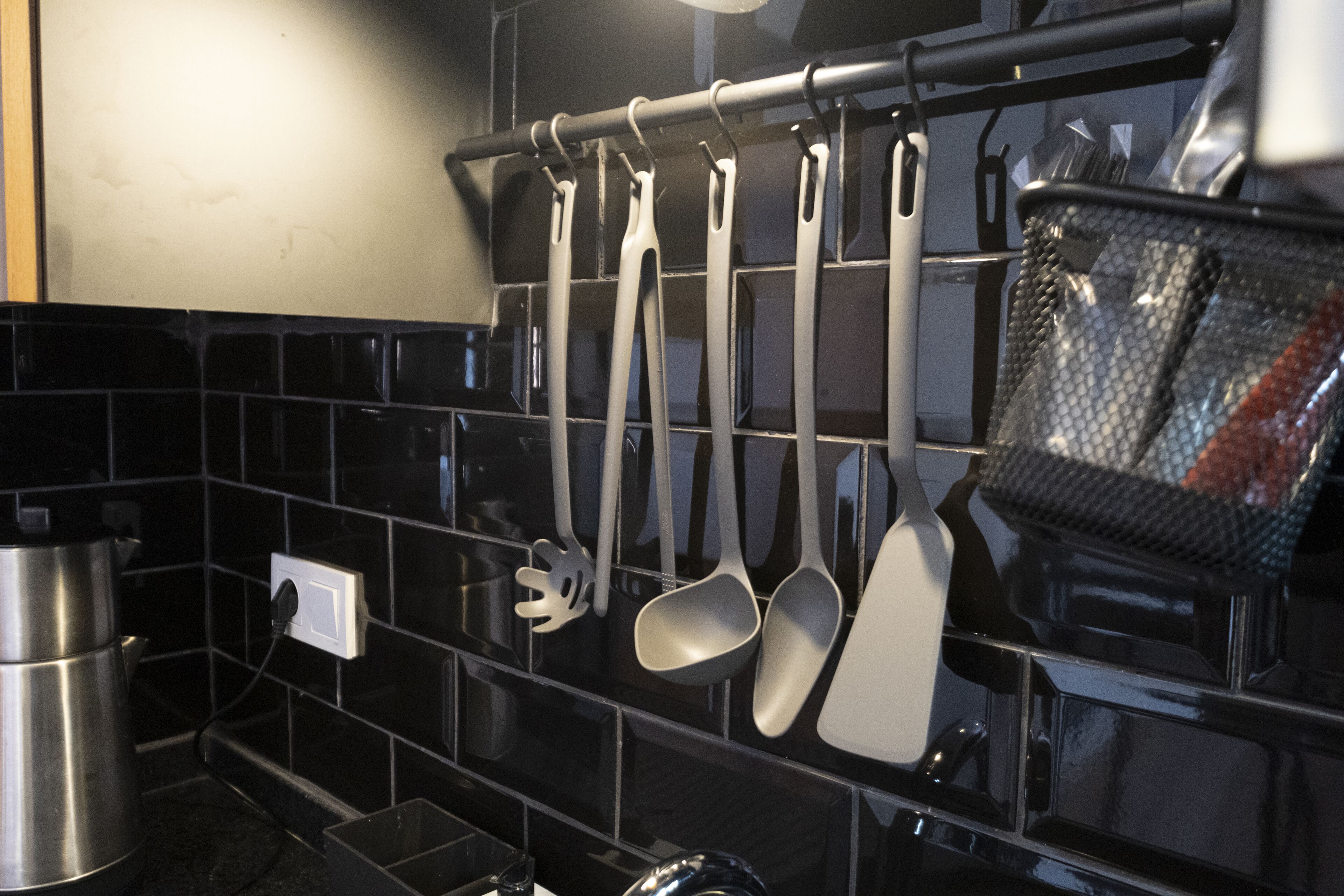 A kitchen with black tiled backsplash, stainless steel appliances, and utensils hanging on a rack.