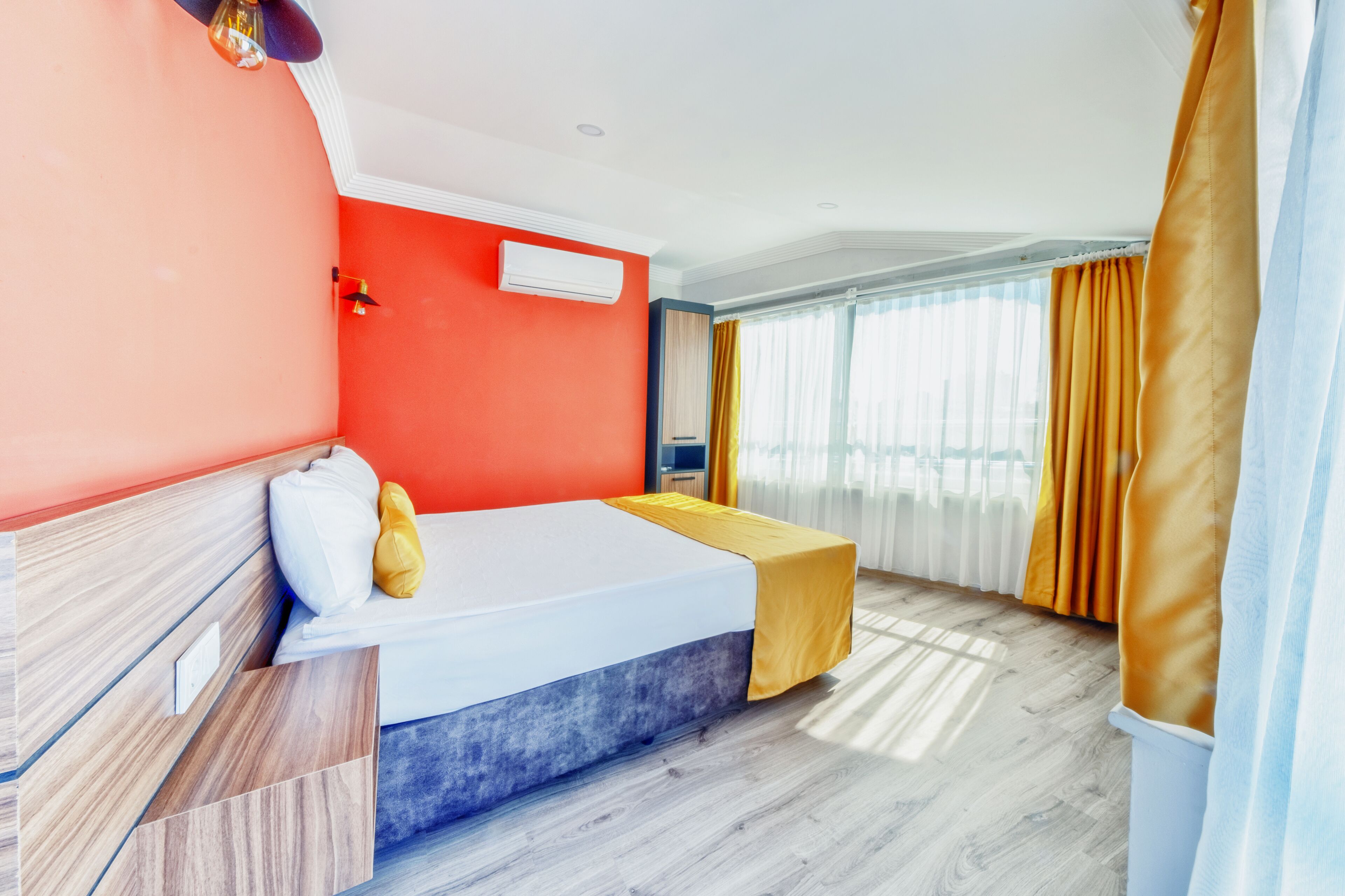 A hotel room with a bed, a bedside table, an air conditioning unit, and curtains.