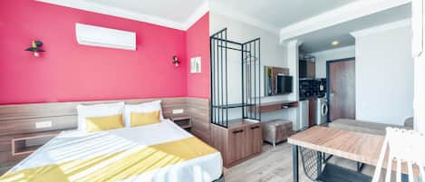 A modern hotel room with a large bed, a dining table, and a kitchenette.