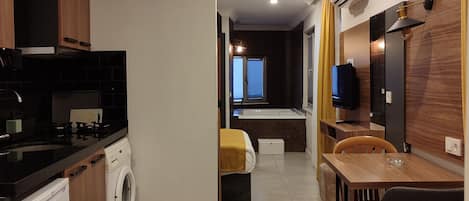 A modern kitchen with a washing machine, a dining area with a table and chairs, and a living space with a sofa and a TV.
