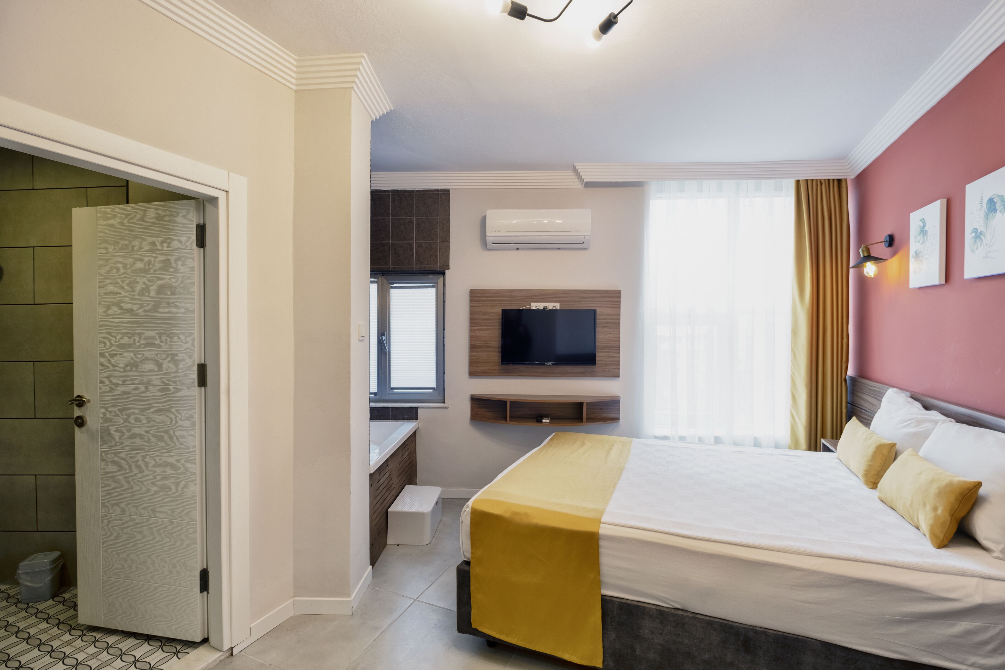 A hotel room with a bed, a television, a window with curtains, and a door.