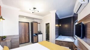 Una habitación de hotel moderna con una cama grande, un baño independiente con bañera, una kitchenette pequeña y un televisor montado en la pared.