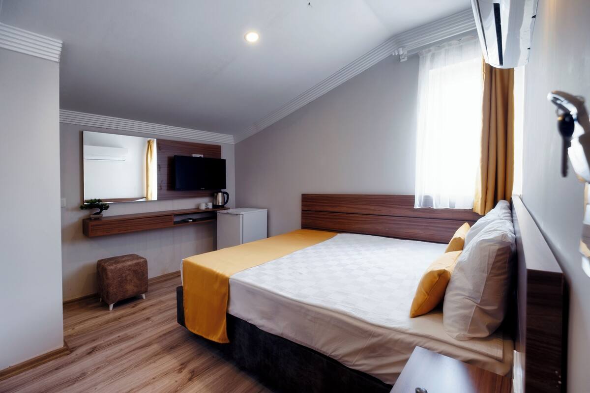 A hotel room with a bed, a desk, a television, and a window with curtains.