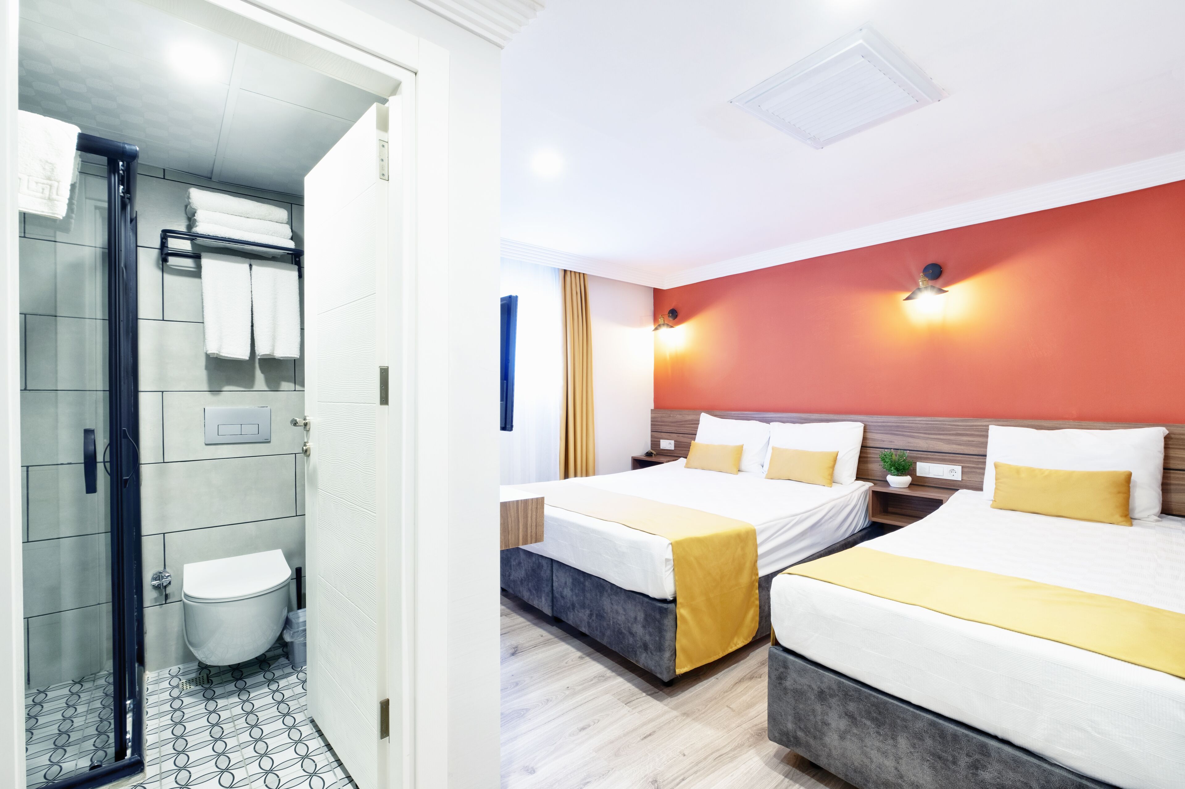 A hotel room with a shower, toilet, two beds with yellow bedding, and a red accent wall.