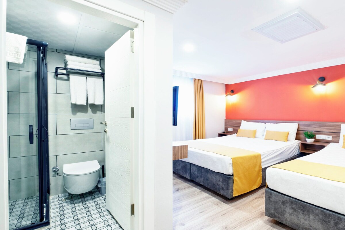 A hotel room with a shower, toilet, two beds, and a red accent wall.