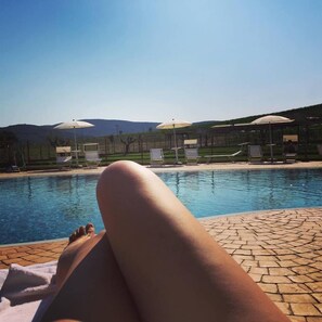 A poolside area with lounge chairs and umbrellas, a clear sky, and a mountainous backdrop. - Cascina al colle (Piombino)