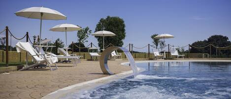 A swimming pool area with lounge chairs and umbrellas.