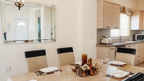 Een eethoek met een tafel voor vier personen, een grote spiegel en een keuken met kastjes en een magnetron.