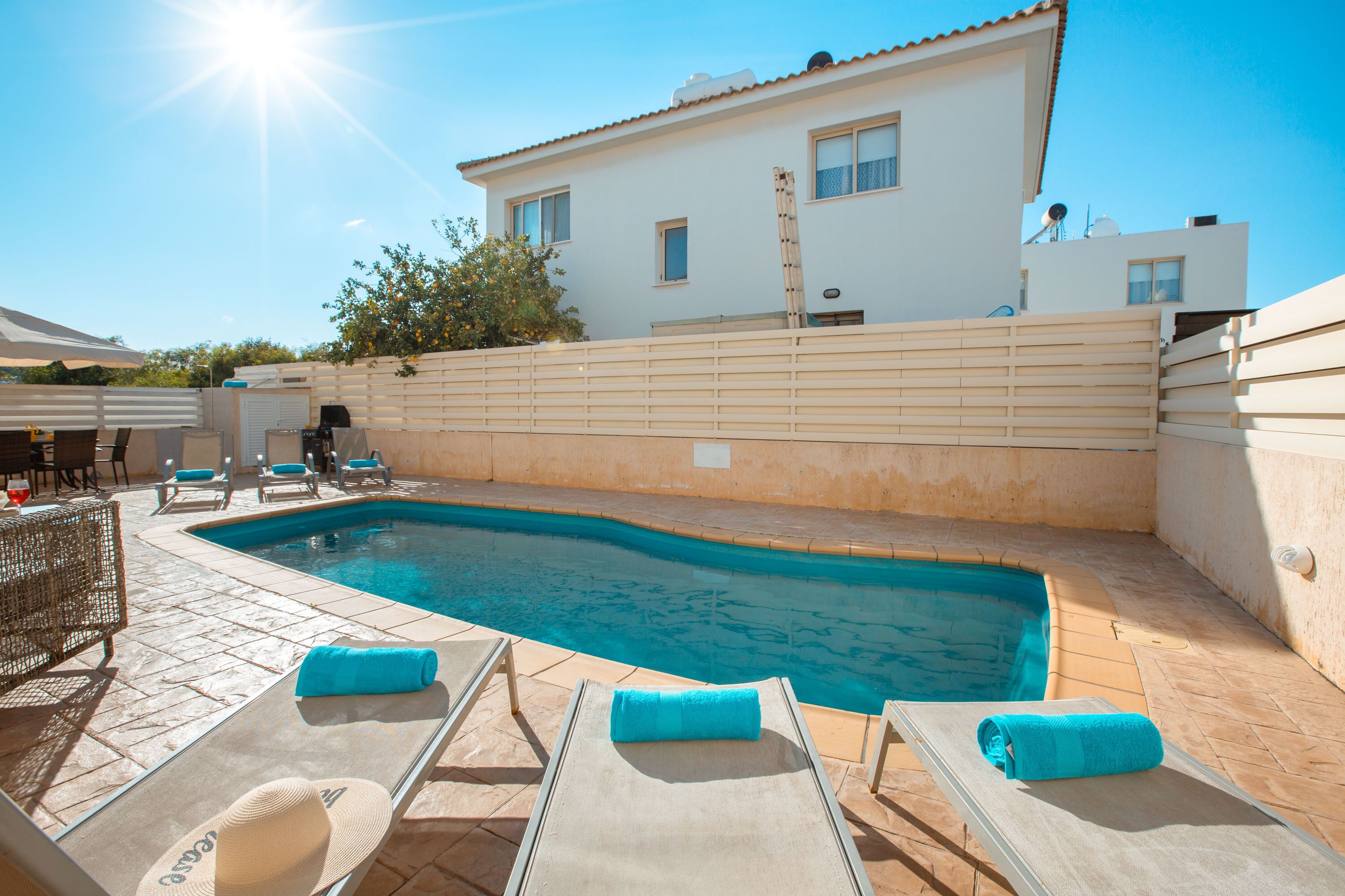 A swimming pool with lounge chairs and a sunbed, a white building in the background, and a clear sky.