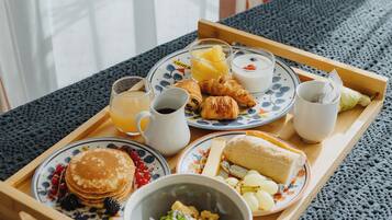 A breakfast tray with pancakes, croissants, fruit, and a bowl of cereal on a wooden table.