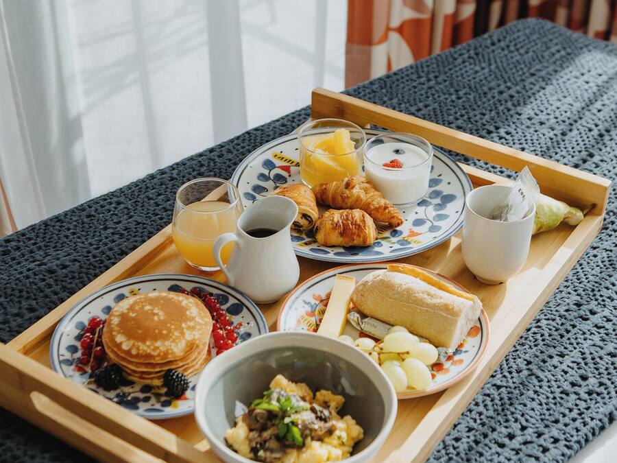 A breakfast tray with pancakes, croissants, fruit, and a bowl of cereal on a wooden table.