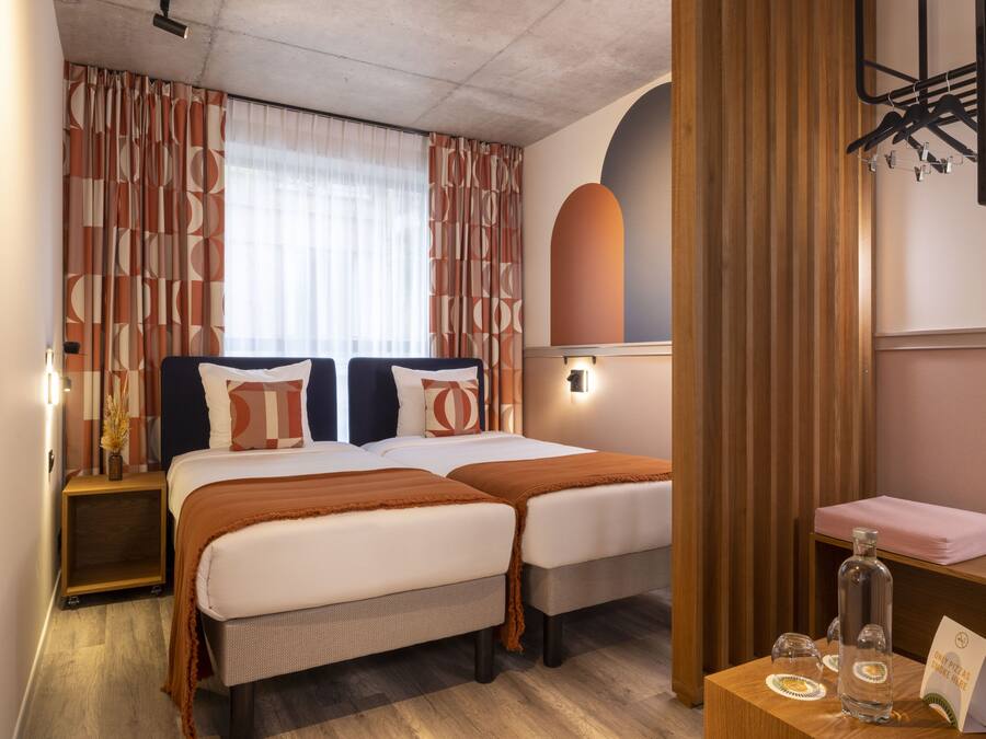 A hotel room with two beds, a wooden headboard, a small table with a bottle and a menu, and a mirror on the wall.