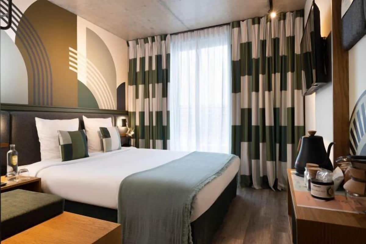 A hotel room with a bed, bedside table, lamp, and curtains.