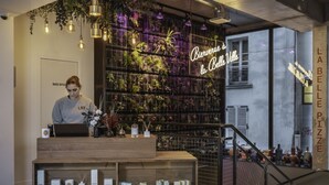 A reception desk with a laptop, a plant, and a shelf with various items. A neon sign reads "Bienvenue à la Belle Ville". - La Belle Ville (Paris)