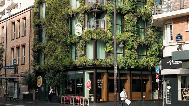 A building with a unique facade covered in greenery, featuring multiple balconies and a ground-level entrance with a sign. - La Belle Ville (Paris)