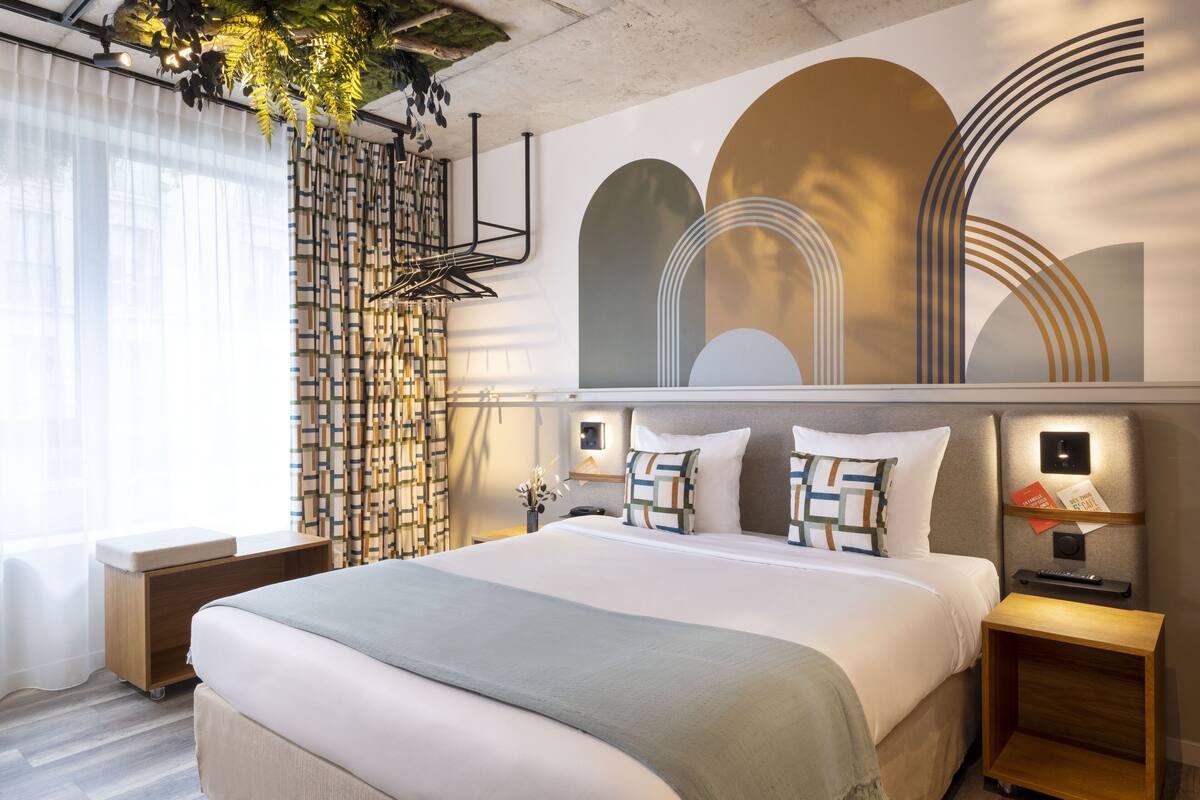 A modern hotel room with a large bed, a bedside table, a nightstand, and a wall with abstract art.